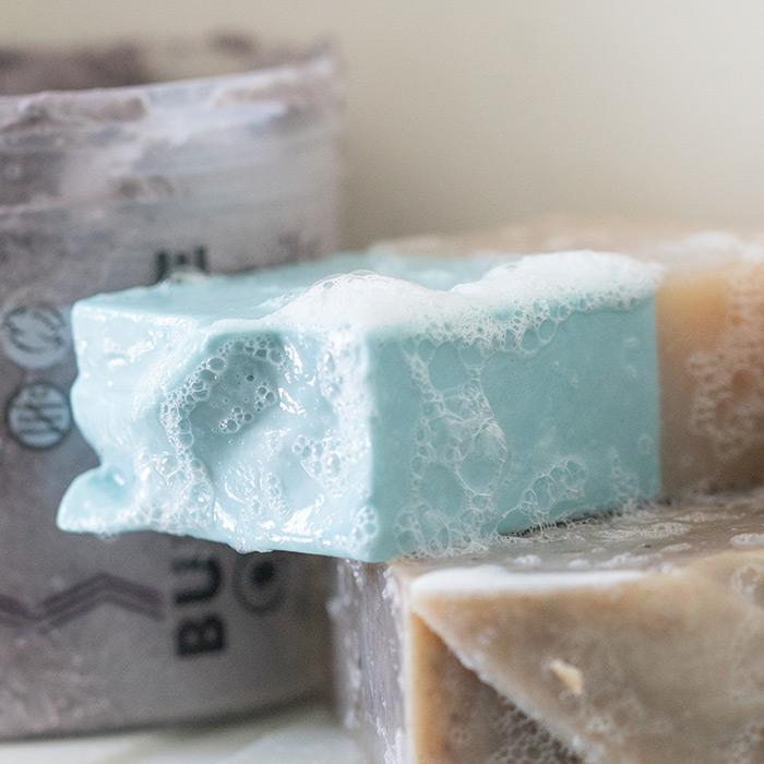 Sand & Sea Bar Soap covered in bubbles sitting on a shower self